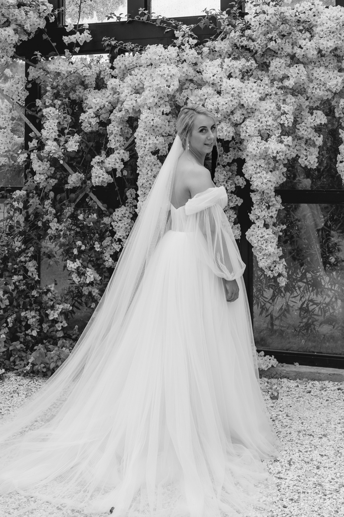 Bride wears off-the-shoulder dress with sleeves.