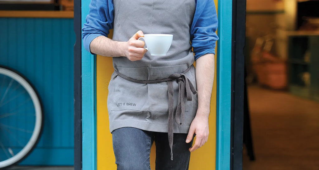Madura stockist wearing Let it Brew apron walking our of cafe with cup in hand