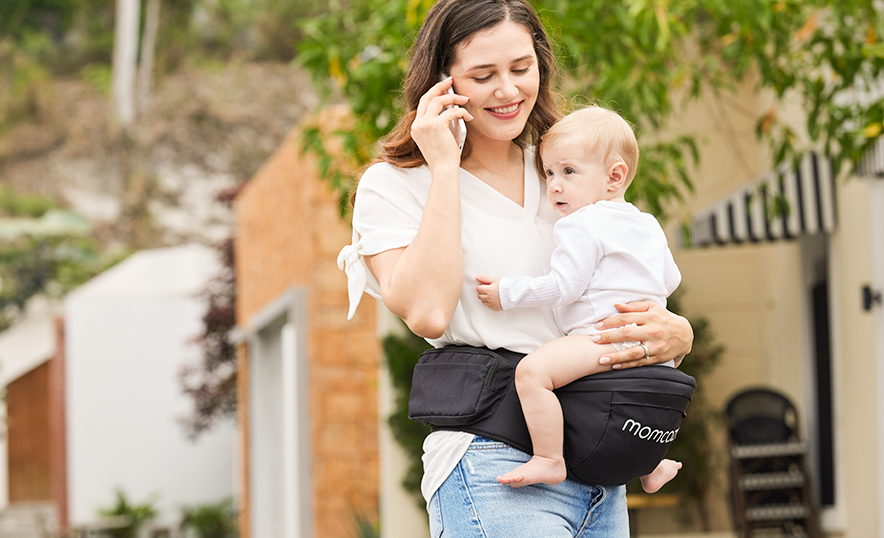 A mom carries her baby with a hip seat carrier