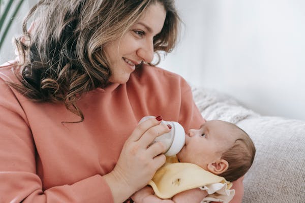 A woman feeds her baby with a warm smile and keeps a healthy fat balance during early childhood