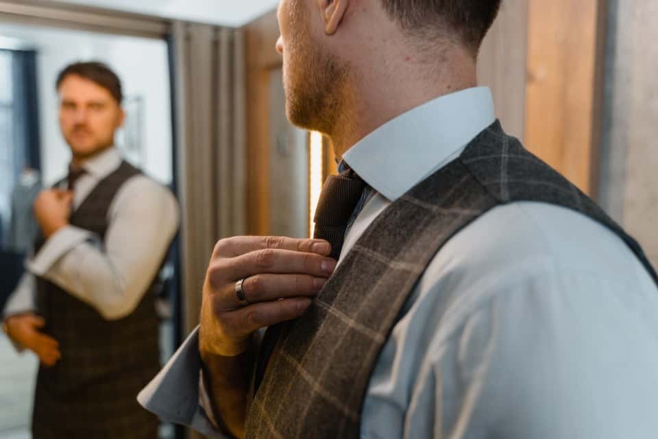 Asortarea vestei la costum - barbat care isi aranjeaza cravata in oglinda