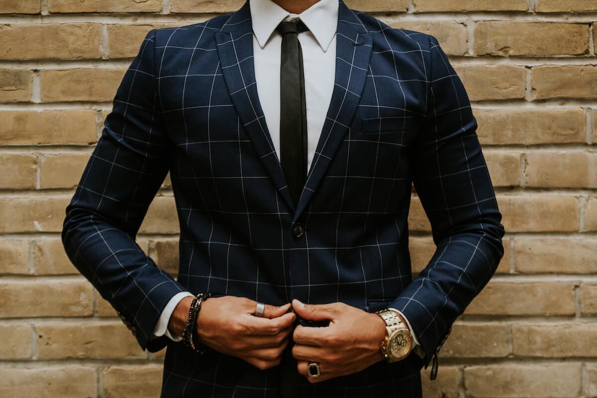 Croieli costume barbati - sacou bleumarin cu linii, cravata subtire neagra, camasa alba, ceas, 2 inele si bratari, fundal cu zid