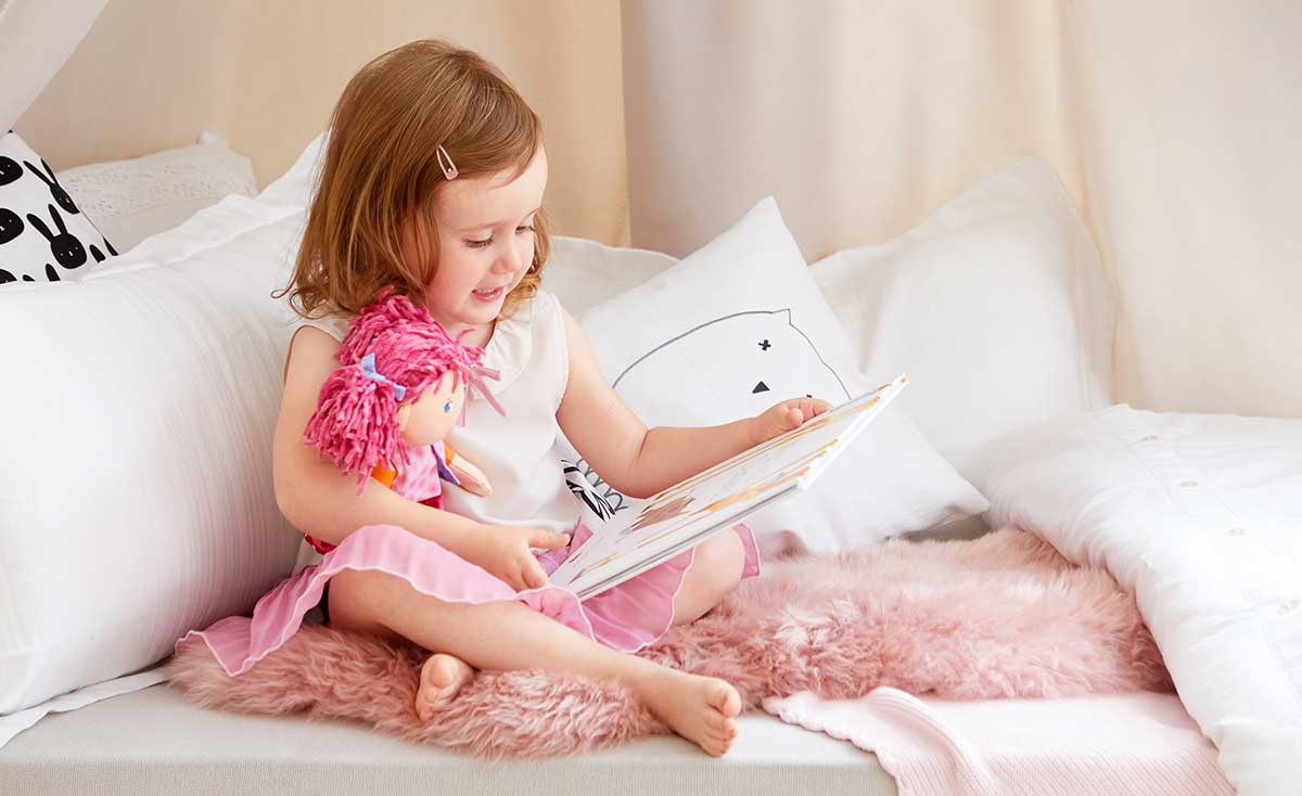 A young girl is reading a book to her HABA soft doll.