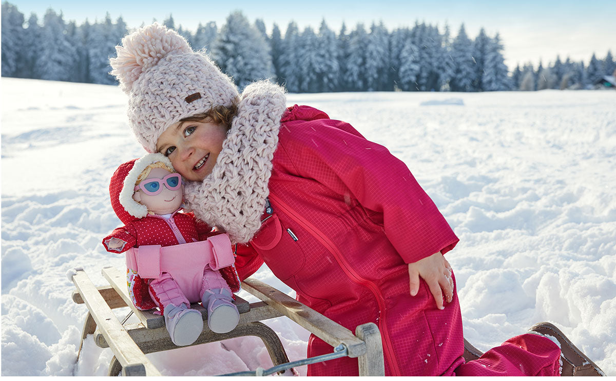 A young girl is playing in the snow with her doll.