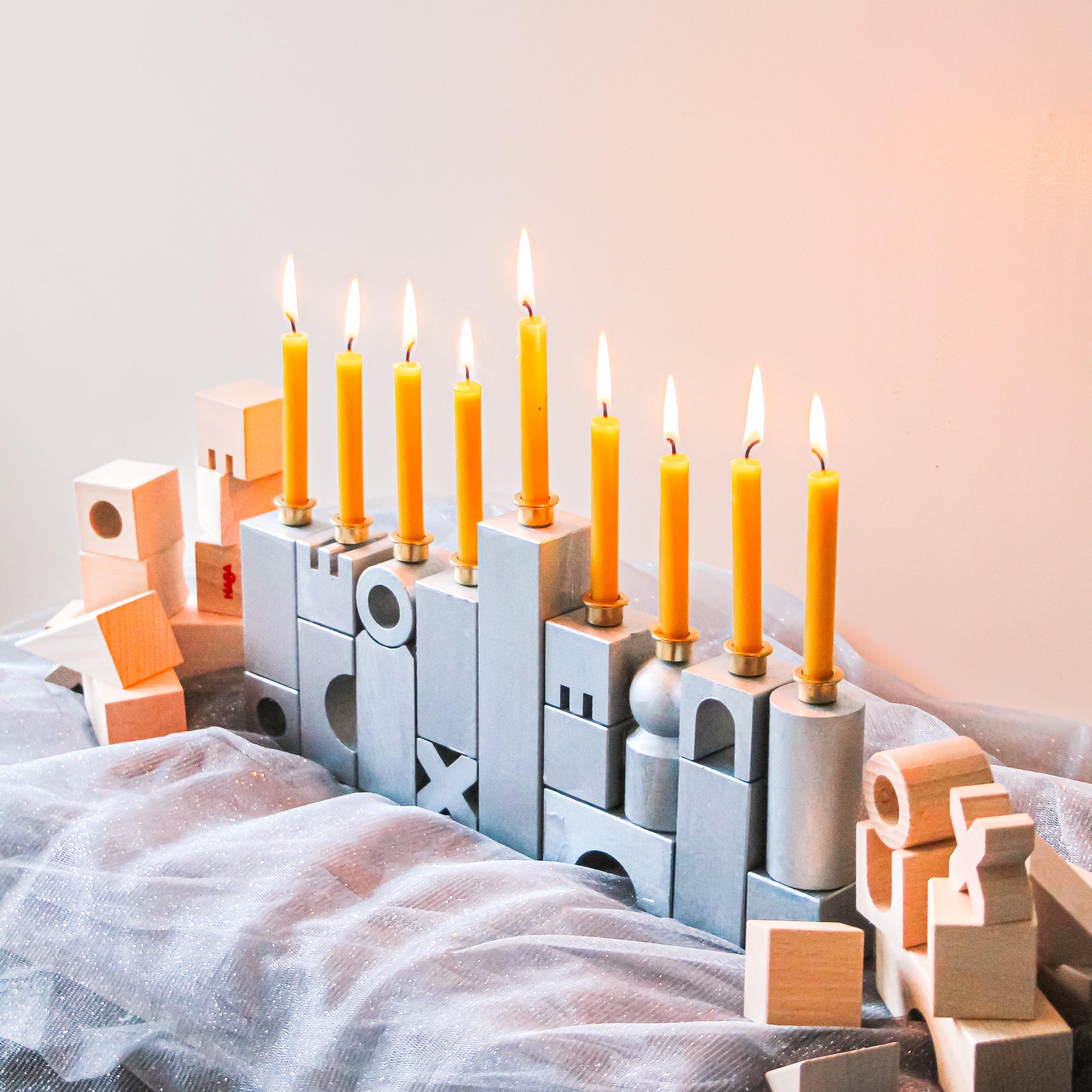 A HABA DIY Block Menorah Sits on a table with unpainted wooden blocks and sparkly fabric.