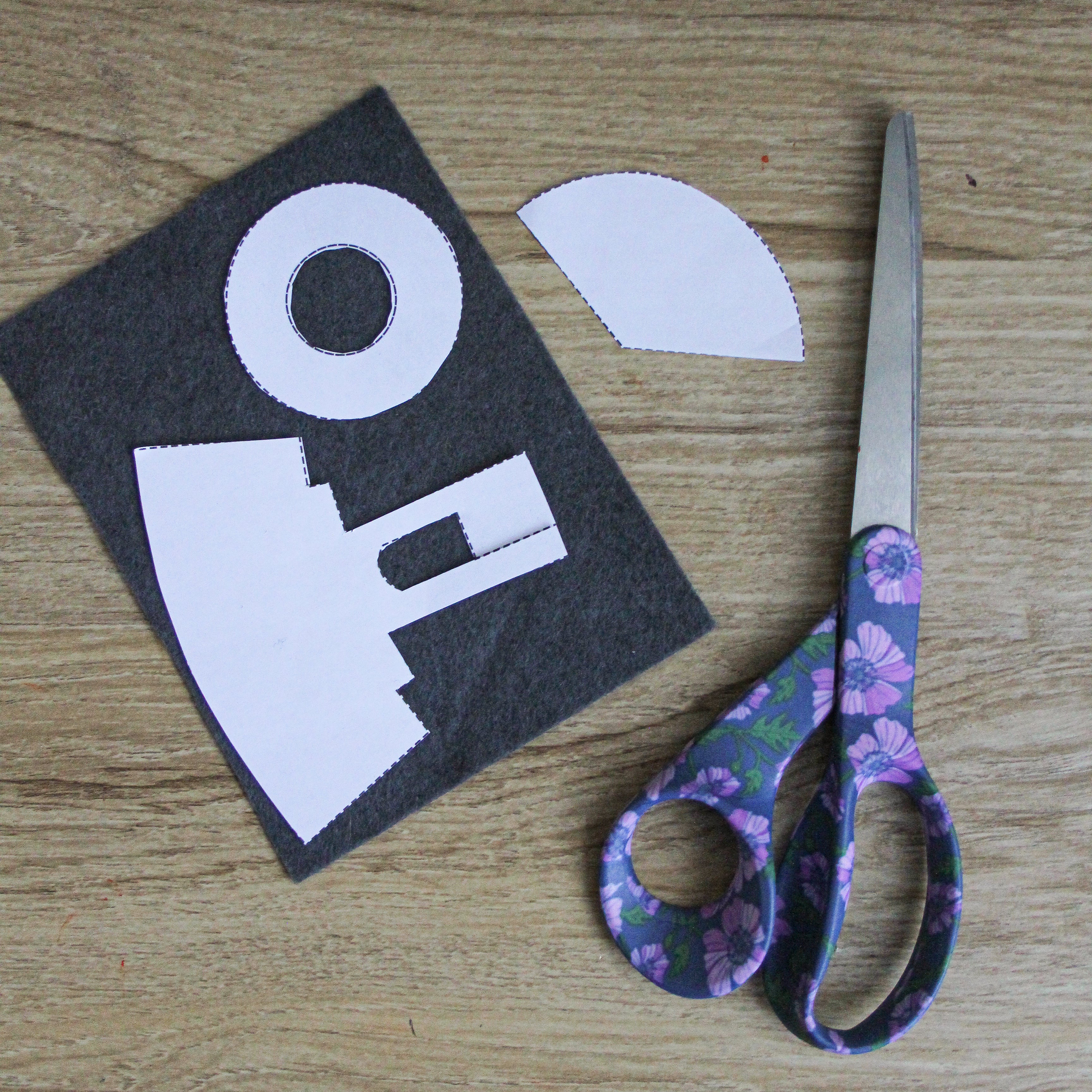 A pair of scissors sit next to paper pattern pieces and a piece of gray felt.