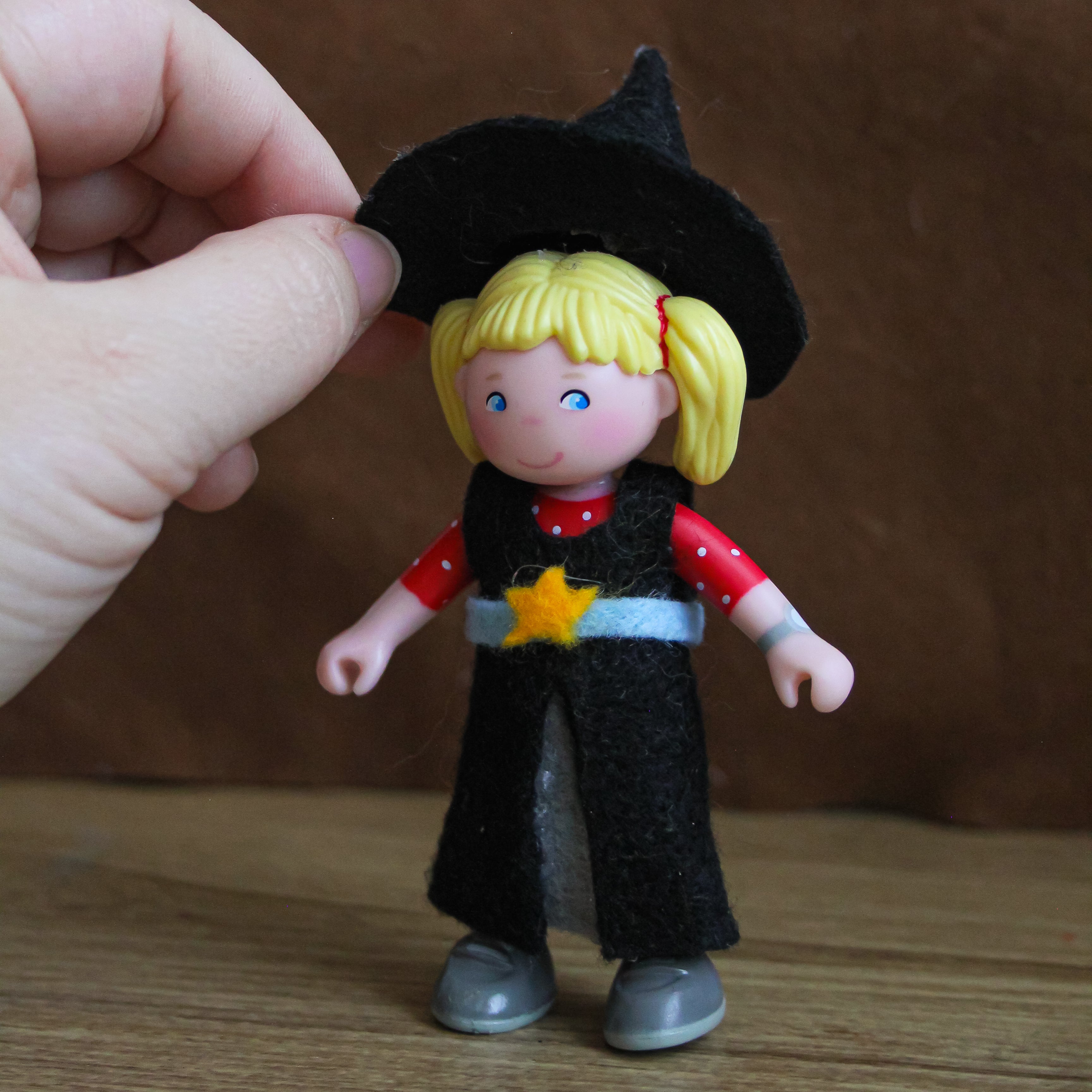 A felt witch costume is being put on a Little Friends Doll.