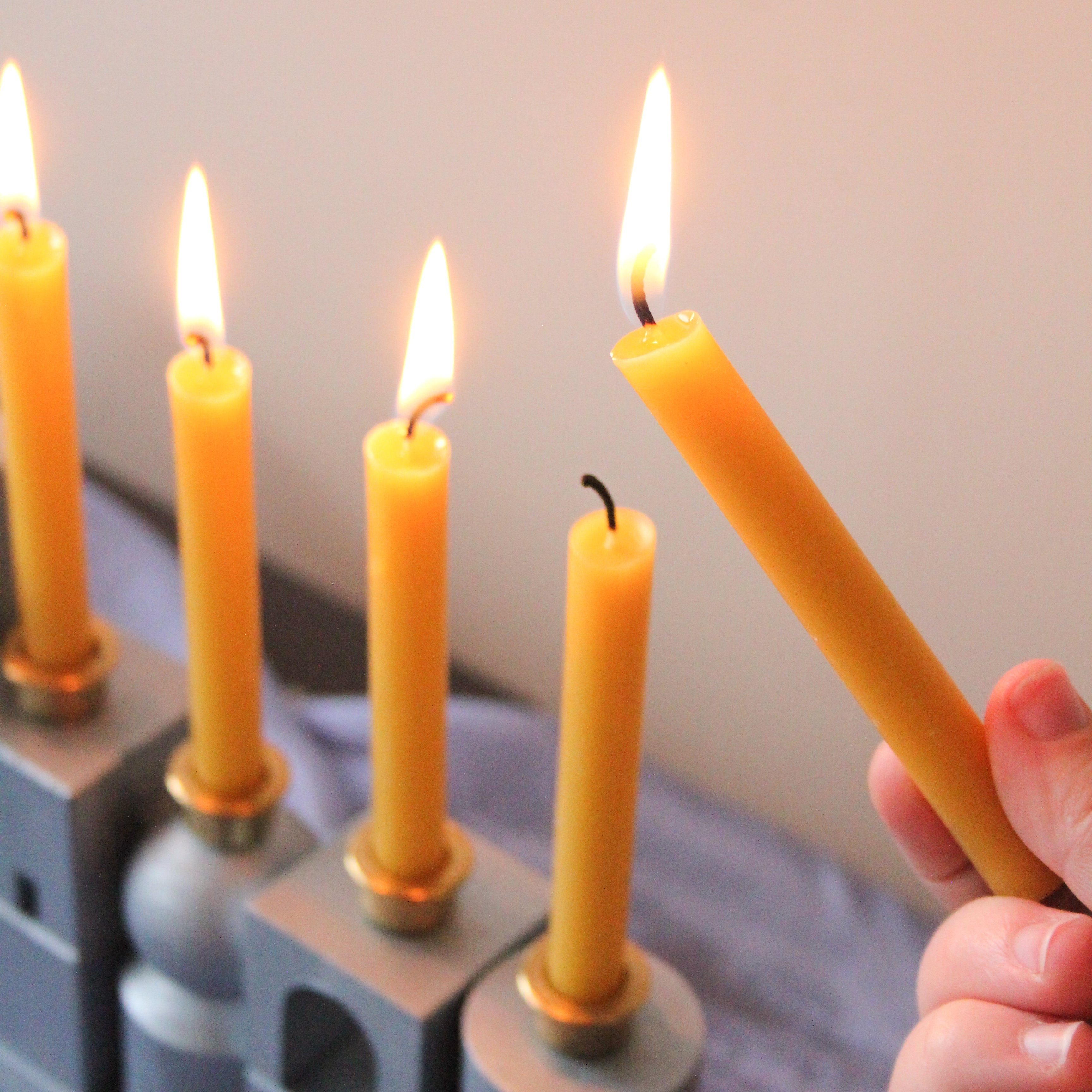 A beeswax candle is being lit in the HABA Block Menorah.