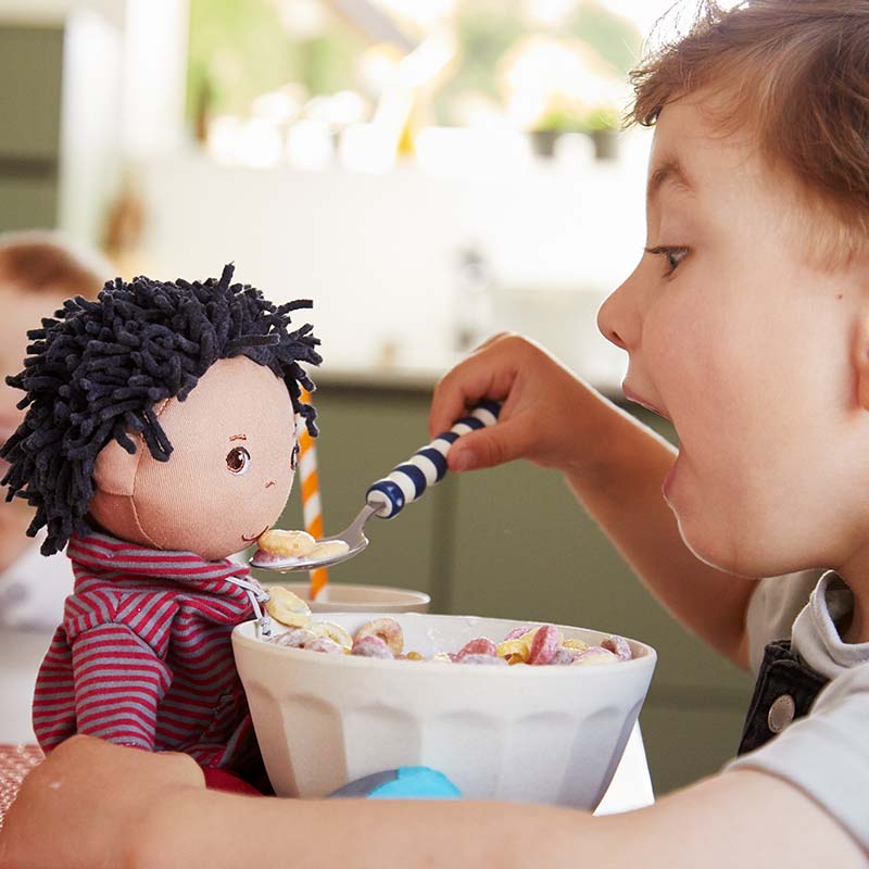 A young oy is feeding his HABA soft doll with a spoon.