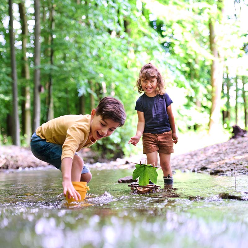 Two kids are playing in the woods with a HABA cork boat.