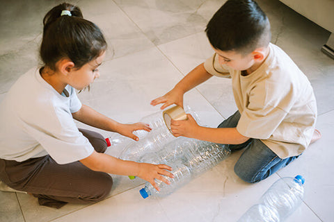 Two kids creating a craft by taping empty bottles together