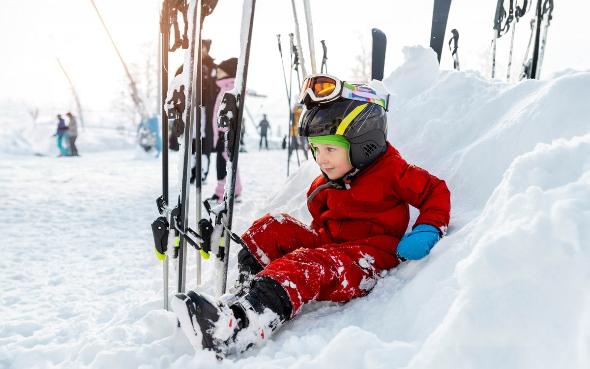 Un bambino seduto nella neve con tutta l'attrezzatura da sci