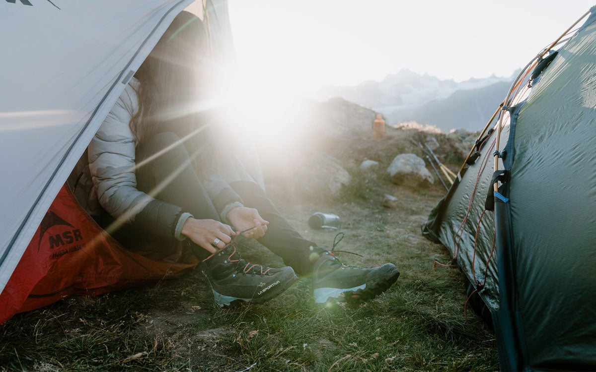 Una ragazza dopo aver passato la notte in tenda si prepara per partire indossando scarponi La Sportiva