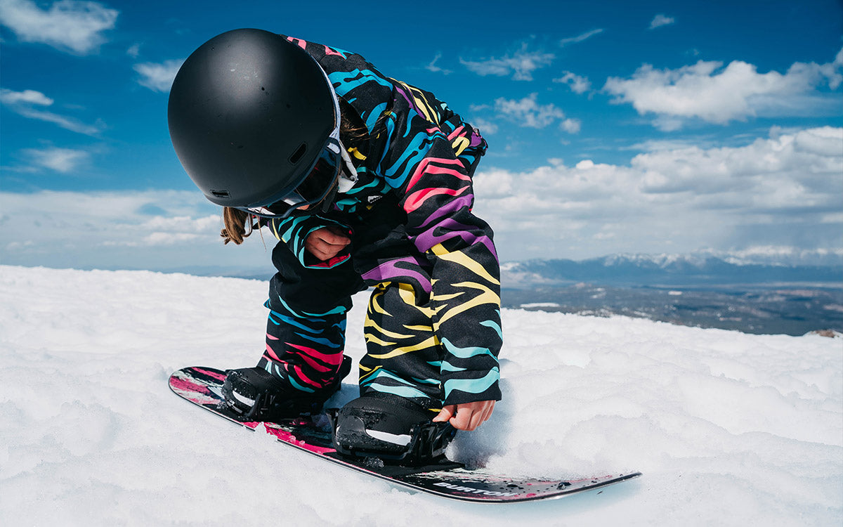 Una bambina mentre sistema scarponi ed attacchi Burton sulla sua tavola da snowboard