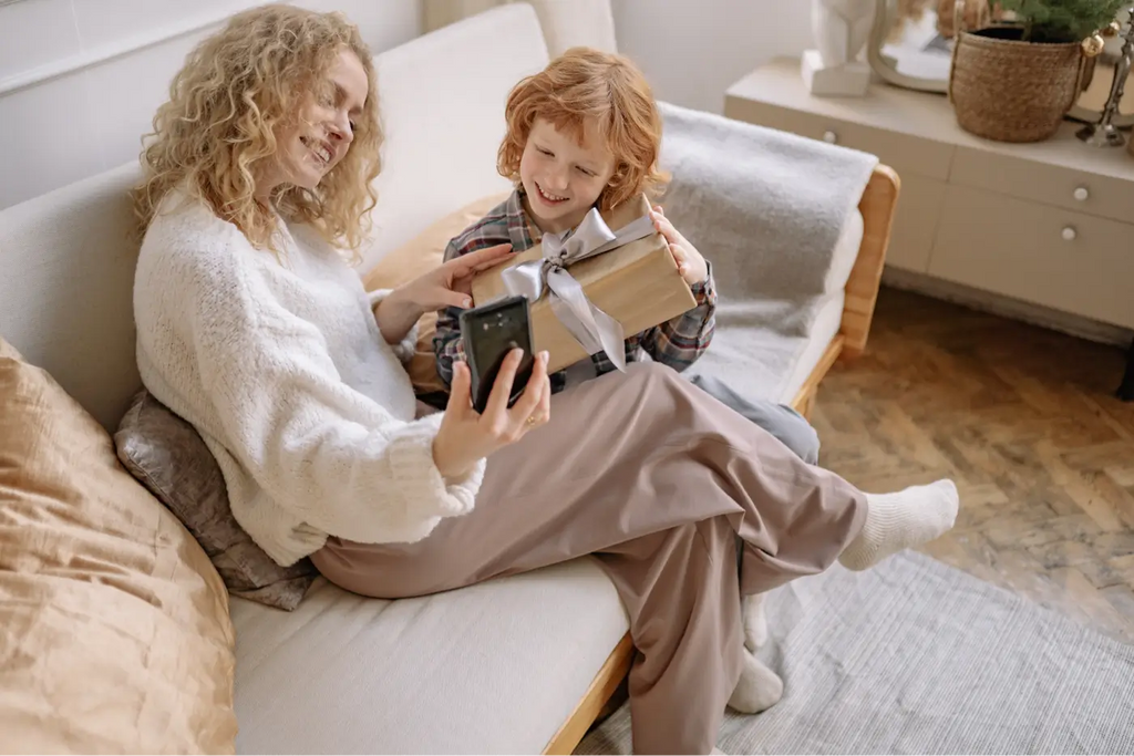 Jeune enfant assis sur une canapé beige qui offre un cadeau à sa maman