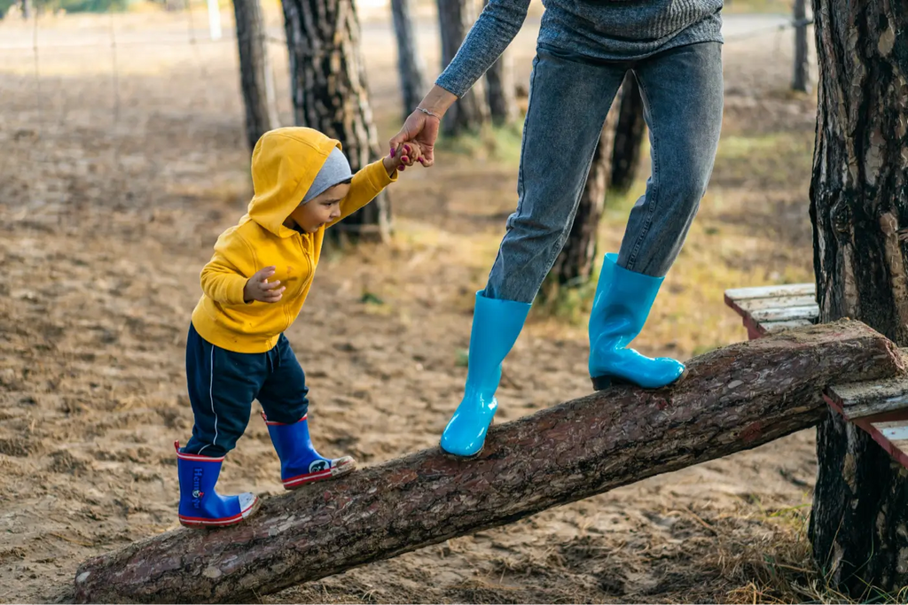 Maman avec son enfant en bottes de pluie qui sont en équilibre sur un tronc d'arbre