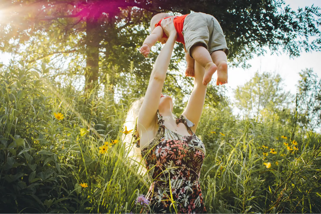 Maman qui joue avec son enfant dans ses bras dans un champ en pleine nature