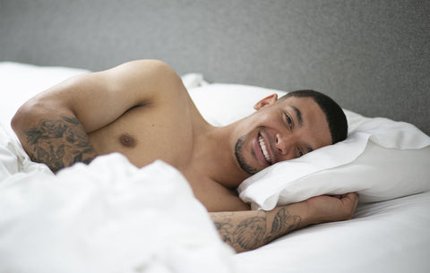 man with tattoos on his arms laying in bed smiling