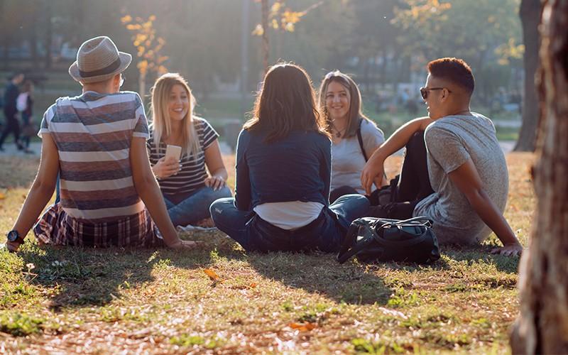 Groep jongeren in een stadspark, zittend in een cirkel op het gras.