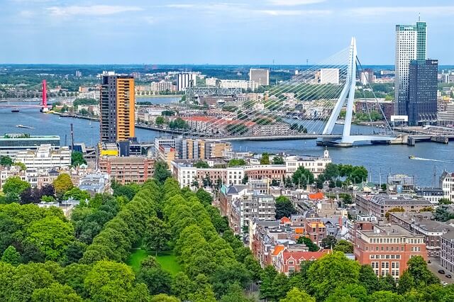 Luchtfoto van Rotterdam met diverse gebouwen zoals woontorens, en de Erasmusbrug op de achtgrond.