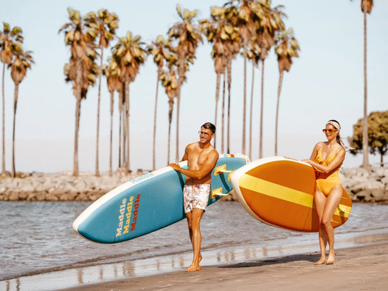 Man and woman carrying paddle boards on beach