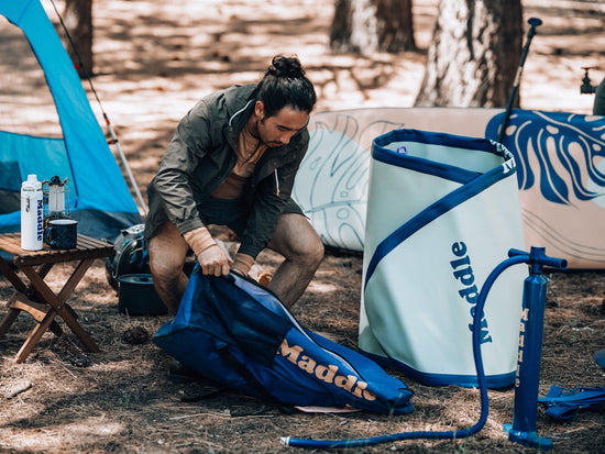 man on campsite in forest with paddle boarding gear