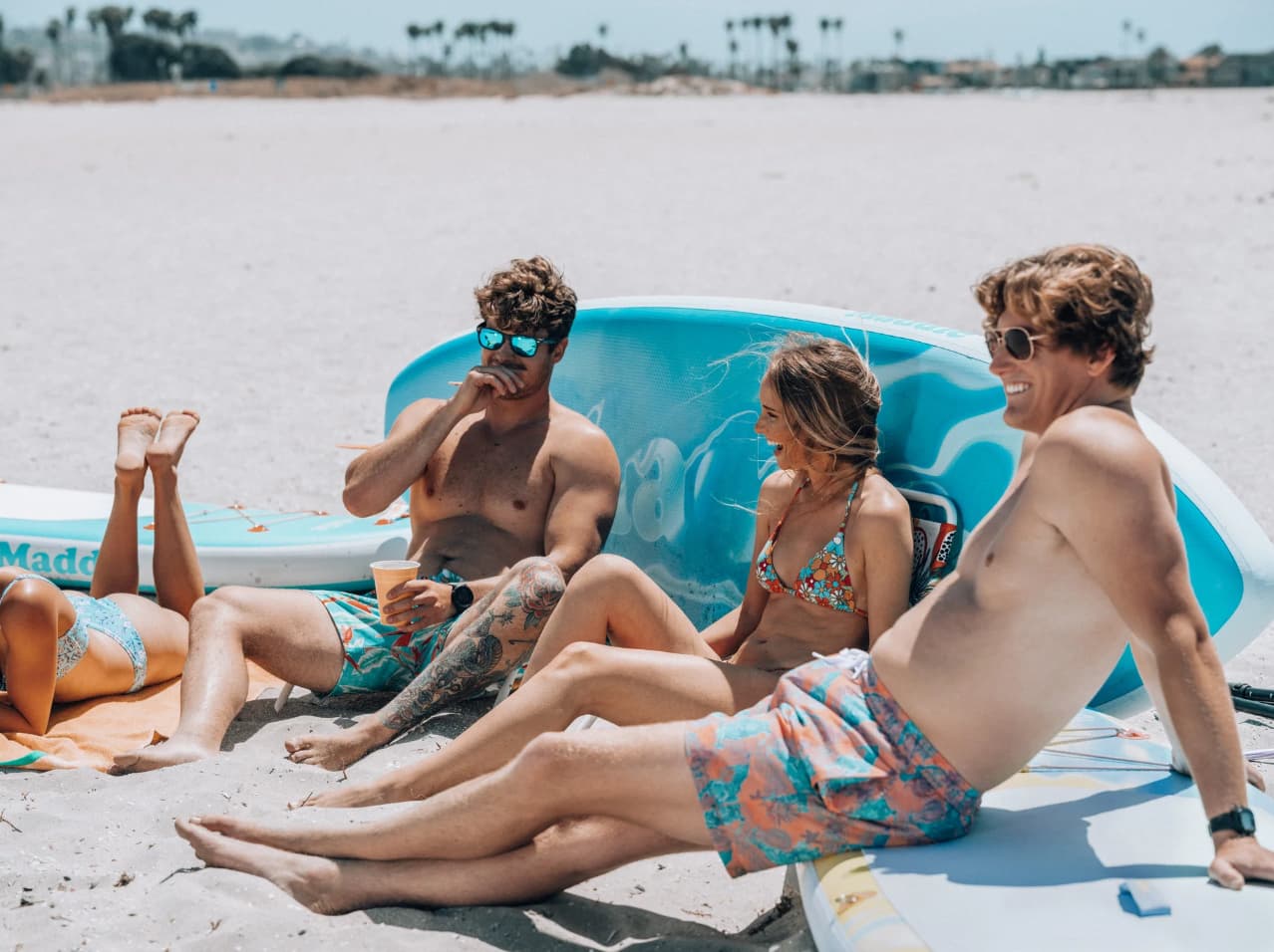 friends sitting on a sandy beach with paddle boards