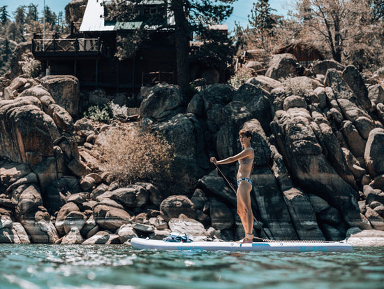 woman on SUP paddling near rocks