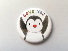 Load image into Gallery viewer, A white round fridge magnet, with a black and white penguin stretching it&#39;s wings up towards the words love you in rainbow colours
