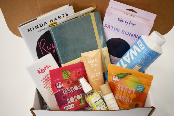 photo of conference welcome kit with snacks, personal care items, a notebook, pen, bonnet, and book in a white box