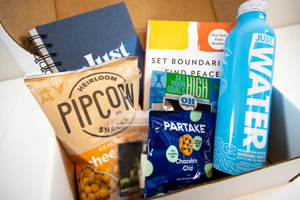 photo of conference welcome box including water, snacks, and skincare items as well as a notebook and a book