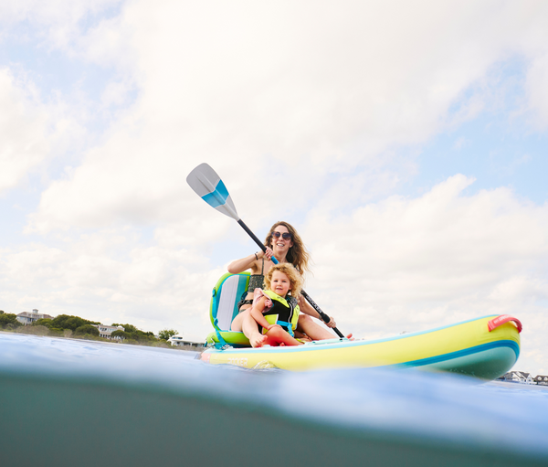 Woman paddle boarding with inflatable kayak seat and daughter