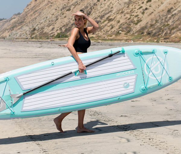 Woman carrying her inflated, light-weight ULTRA standup paddleboard on the beach