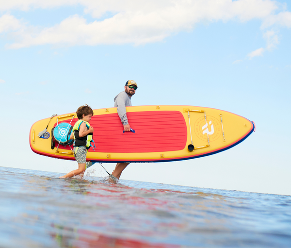 Man walking with paddle board and kid on a beach