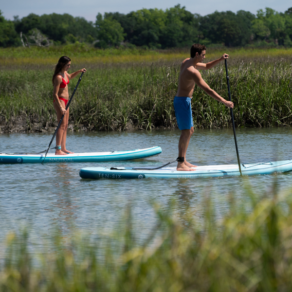 Man and woman paddling on their boards in a marshy creek.