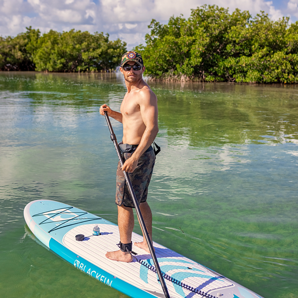 Woman carrying BLACKFIN standup paddle board on rocky shoreline