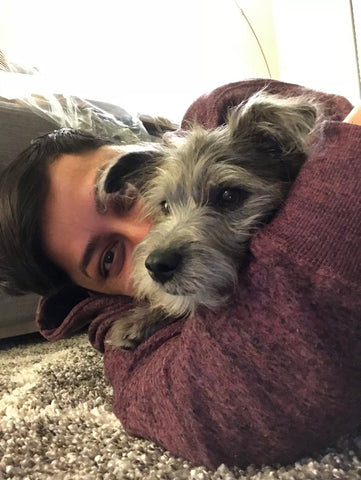 Woman in red sweatshirt laying on the floor and bear hugging her little furry grey puppy