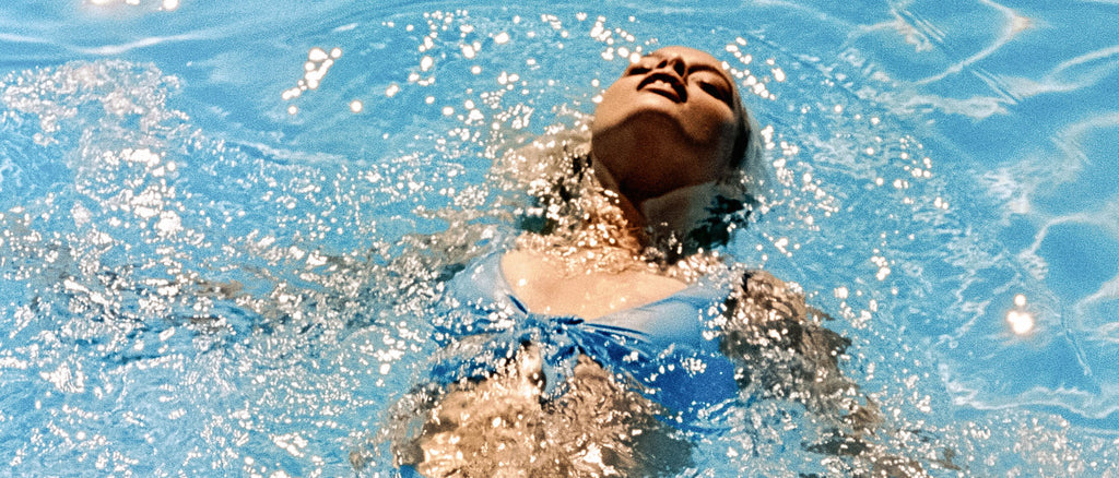 Blondes Mädchen mit kleinen Brüsten in Badebekleidung schwimmt im Pool.