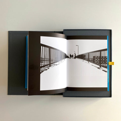 Collectable book is laid open revealing a black and white photo spread across two pages. The clamshell case this limited edition comes in sits underneath the book