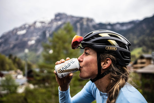 Cycling women drinking a Thrive sports beer with mountains in the background.
