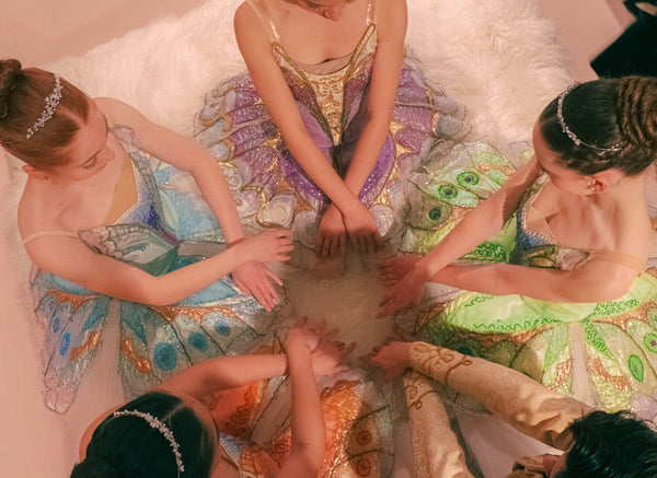 5 ballet dancers sitting with hands crossed