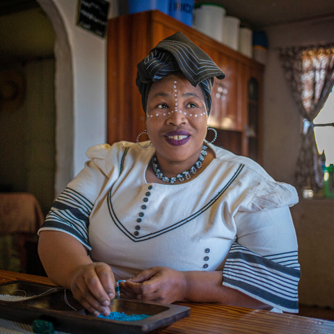 Woman beading with plate of beads in front of her and needle in her hand