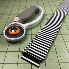 rotary cutter and strips of black and white fabric on cutting mat