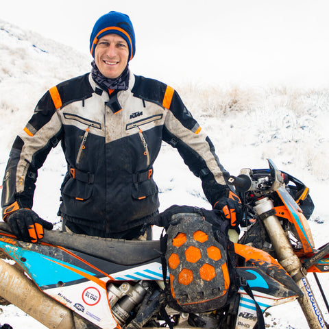 Motorcyclist standing behind his KTM dirtbike in the snow, with a Kriega Trail9 featured