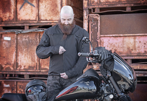 Male motorcyclist zipping up his Speed and Strength motorcycle jacket, while standing behind his motorbike