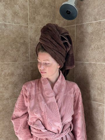 woman in pink robe with hair wrapped in towel to prevent hair shedding