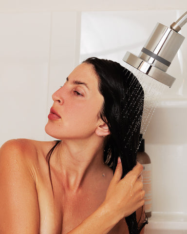 woman with dark hair using showerhead for seasonal hair shedding