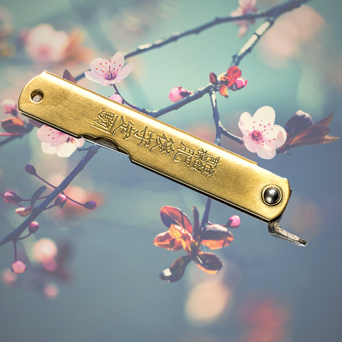 A Japanese knife, possibly Higonokami in the foreground with a cherry blossom in the background