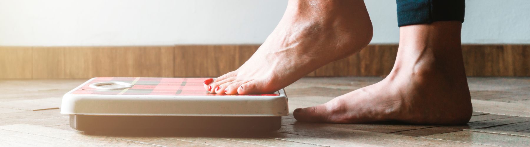 A person stepping onto a weighing scale, an example of what should a good weight management program include.