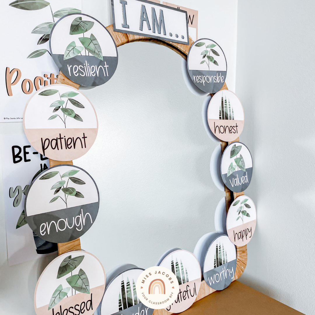 Two images are shown. On the left a graphic shows some of the elements of the Affirmation Station Display. We see illustrated plants in camel, green and blue-gray tones. The words caring, happy, honest, brave, strong and kind are shown. On the right we see the display created in an office setting - an arch shaped mirror is surrounded by circular affirmations each with a plant illustration. The top of the mirror says ‘I am’ and the affirmations include enough, patient, a leader, grateful and happy.